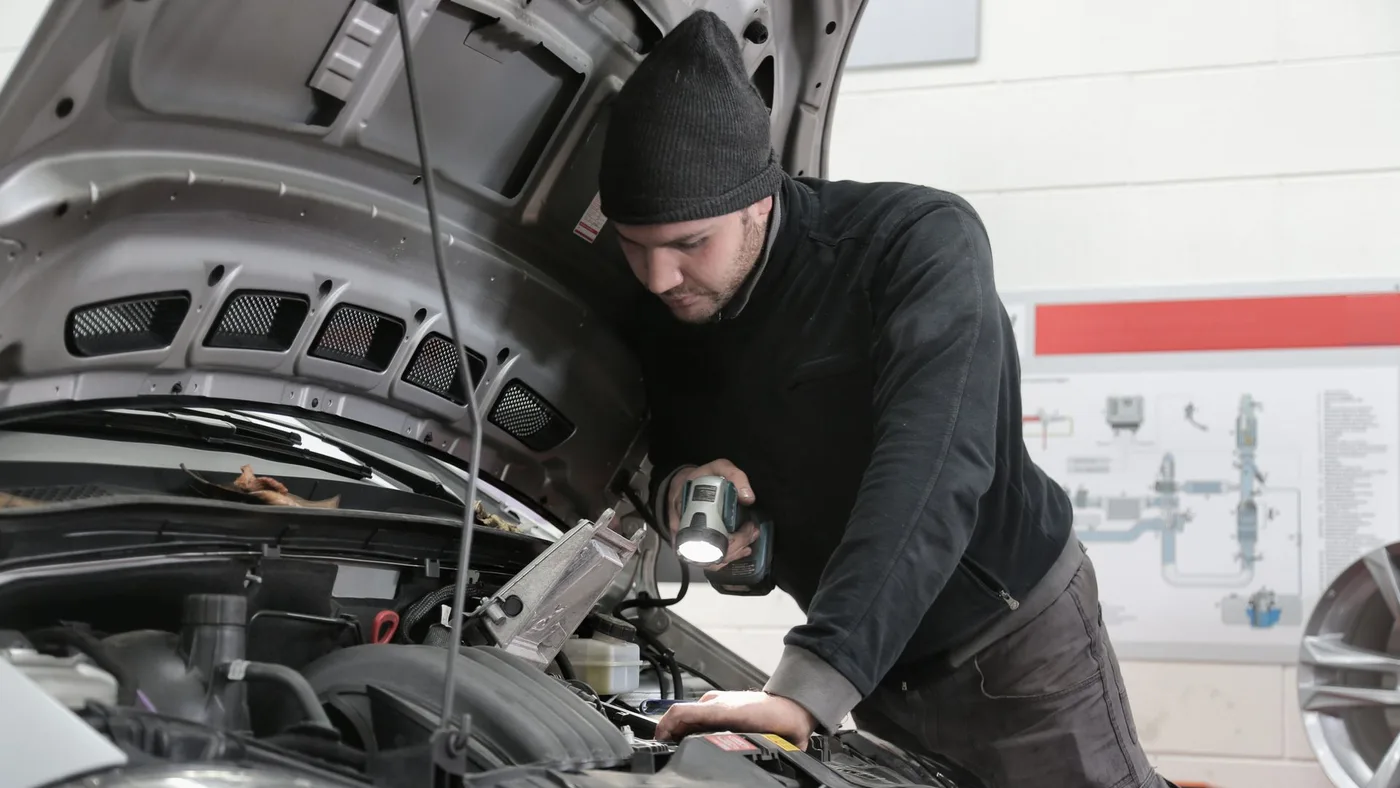 Technician using a work light to inspect an open car engine bay in a repair workshop