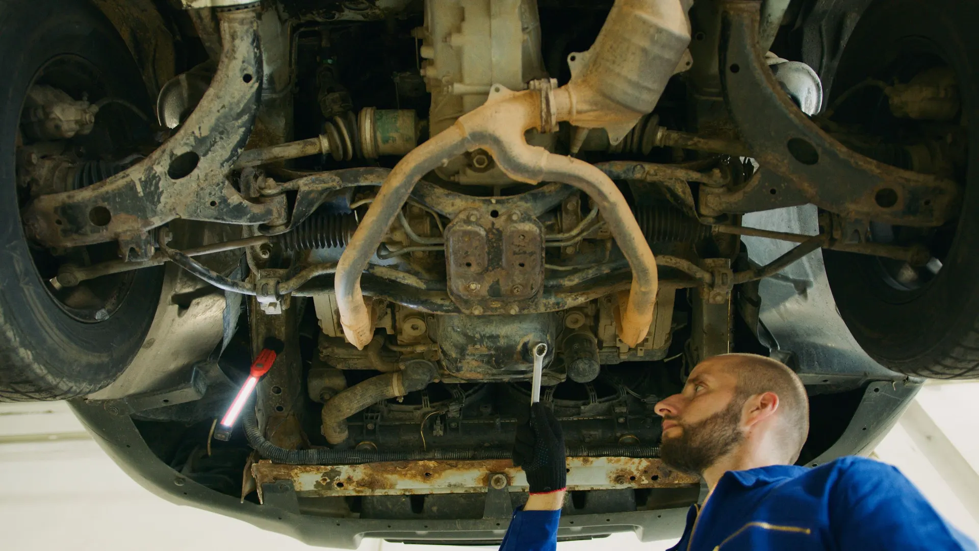 Technician working beneath a vehicle raised on a lift in an automotive repair shop
